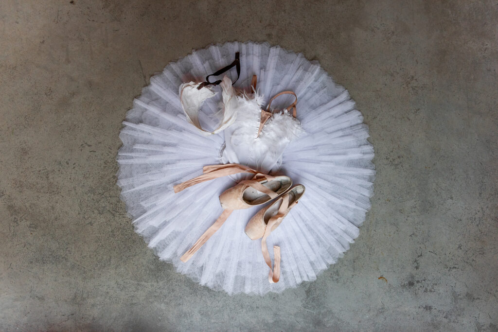 Top view of a white ballet tutu, pointe shoes, and feathered costume laid on the floor showing how ballet costumes changed from stiff, formal wear to lightweight designs that support freedom of movement.